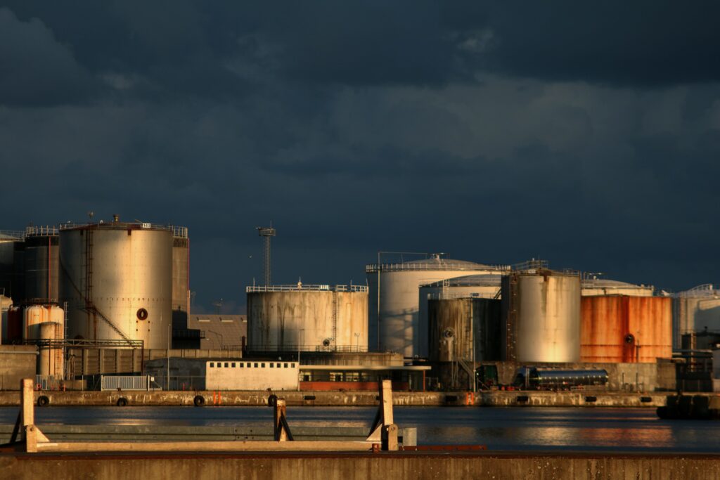 Storage tanks at a port terminal lit by low sun under a dark sky