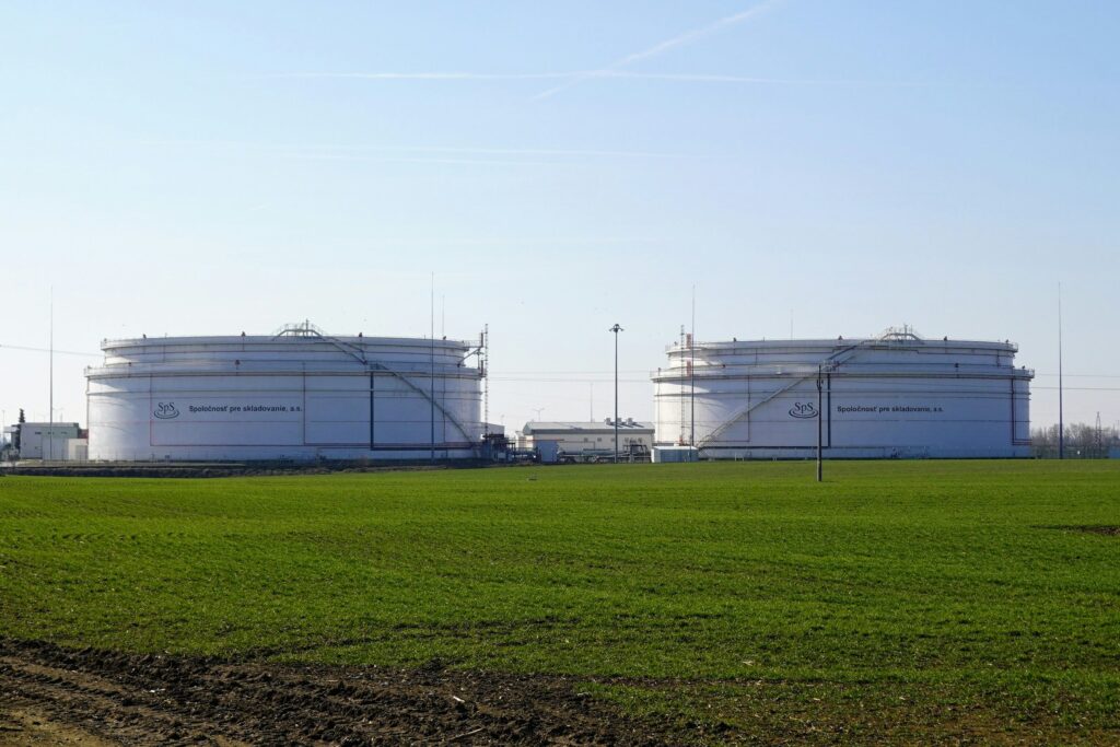 Large white bulk storage tanks beside an open green field